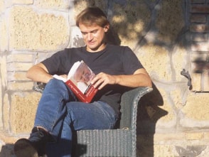 Andreas Englisch in einem Stuhl wie er sein Buch "Johannes Paul II" liest, während links neben ihm ein Hund schläft.